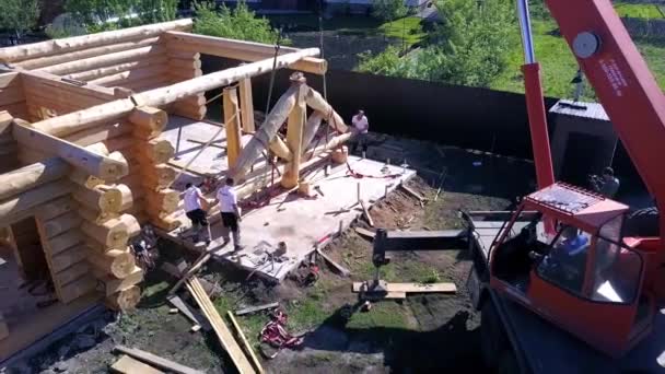 Vinçli işçiler evin ahşap yapısını kaldırıyor. Şarjör. İşçilerin ve vincin yardımıyla ahşap çatı cephesi kurma sürecinin en üst görünümü — Stok video