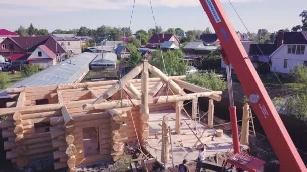 Jeřáb zvedá na kabelech dřevěnou konstrukci. Klip. Horní pohled na proces výstavby dřevěného venkovského domu s jeřábem. Návrh jeřábových výtahů fasády dřevěné střechy — Stock video