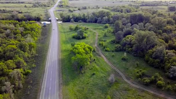 Ovanifrån av motorvägen med bilar på grön bakgrund. Klipp. Track passerar genom gröna träd på bakgrunden av fält når horisonten. Panorama motorväg med rörliga bilar på sommaren — Stockvideo