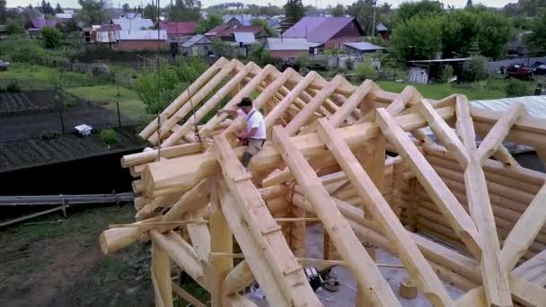 Arbeiter bauen auf dem Dach eines Holzhauses. Clip. Blick von oben auf Arbeiter, die Dachstuhl eines hölzernen Landhauses bauen. Arbeiter arbeiten während des Hausbaus in luftiger Höhe — Stockvideo