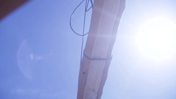 Crane with log for construction of wooden house. Clip. Suspended timber on crane ropes weighs on blue sky background with sun rays — Stock Video