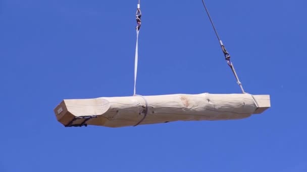 Kraanvogel met log op achtergrond van de lucht. Een knip. Log wordt verplaatst met kraan op bouwplaats voor houten huis. Op de achtergrond van blauwe lucht slepen logs opgehangen aan touwen van de kraan — Stockvideo