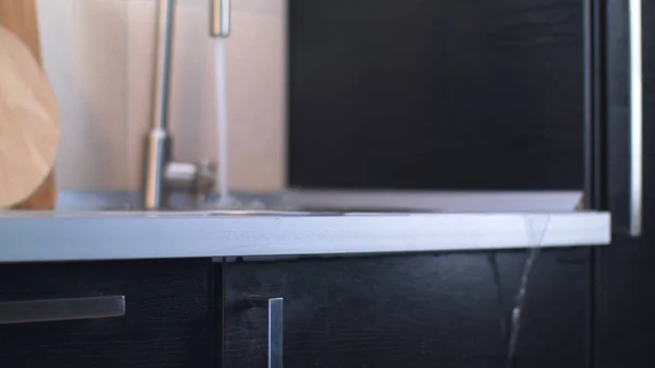 Närbild av den tilltäppta diskbänken med det klara vattnet som rinner från kranen över kanten på golvet i köket. Lagerbilder. Problem med vattenförsörjningen. — Stockfoto