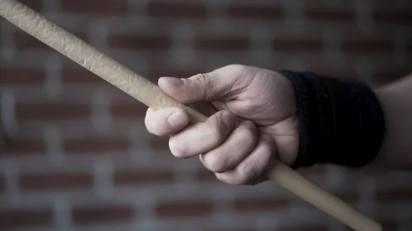 Gros plan de la main de l'homme avec bracelet en tissu noir sur son poignet tenant le tambour et le tournant à l'aide de ses doigts sur un fond de mur de brique rouge. L'action. Concept d'instruments de musique . — Photo