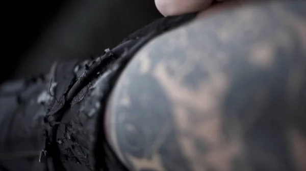 Närbild av den manliga armen med svart tatuering och en man som sätter på svart gammal arm varmare, konst koncept. Börja. Man med en stor tatuering på armen drar upp svart tyg arm varmare. — Stockfoto