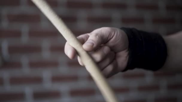 Close up of man hand with black fabric bracelet on his wrist holding drumstick and rotating it with the help of his fingers on a red brick wall background. Action. Musical instruments concept. — Stock Video