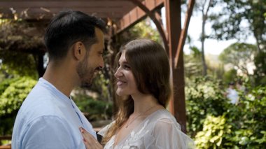 Yeni evliler bahçede birbirlerine sevgiyle bakarlar. Başla. Güzel genç çift, güneşli yeşil bahçede birbirlerine sevgiyle bakıyor.