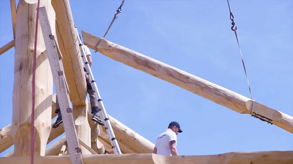 Grue avec bois et travail sur chantier. Clip. Vue du bas du procès de la construction du bâtiment en bois. Travailleur sur le chantier dirige grue avec bûche — Photo