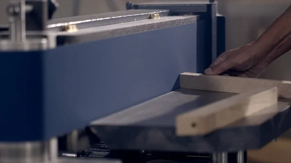 Close-up of man grinds wood products on industrial machine. Action. Carpenter polishes wooden product for tape manufacturing machine — Stock Photo, Image