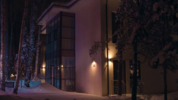 Fassade des großen Hauses am späten Winterabend vom bunten Blaulicht eines Einsatzfahrzeugs beleuchtet. Archivmaterial. Blick auf die Hütte im verschneiten Winter in der Nacht. — Stockfoto