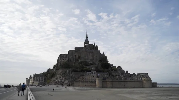 Mont Saint Michel, uma ilha rochosa na Normandia, França, é a sede do mosteiro de Saint-Michel. Acção. Pessoas que visitam castelo bonito e famus no fundo azul céu nublado . — Fotografia de Stock
