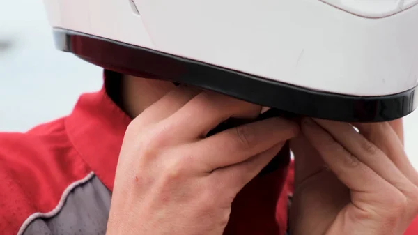 Extremo primer plano de un hombre tratando de quitarse el casco protector blanco en el fondo del cielo brillante. Medios. El joven está tratando de desabrochar su casco de seguridad para quitárselo. . — Foto de Stock