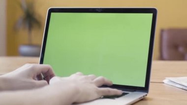 Bir adam evde çalışıyor ve yeşil ekran, iletişim ve iş konsepti olan bir dizüstü bilgisayar kullanıyor. Stok görüntüleri. Krom anahtarla bilgisayarda yazan adam..