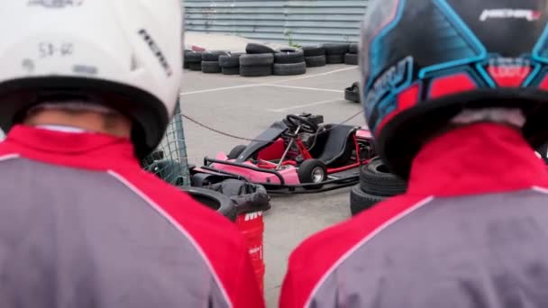 Close up of racer backs wearing special uniforms and helmets going to the kart cars, competition and race concept. Media. Rear view of two men before the karting race. — Stock Video