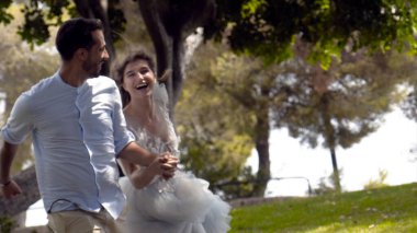 Yeni evliler yazın parkta koşarlar. Eylem. Güzel sevgi dolu çift romantik parkta el ele tutuşarak kaçmak. Beyaz elbiseli karısı kocasını güneş ışığıyla aydınlatarak tutuyor
