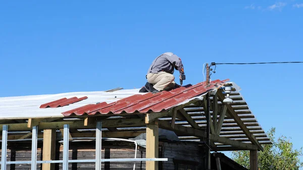 El hombre atornilla un tornillo en el techo. Imágenes de archivo. El trabajador profesional trabaja en la instalación del techo del techo por las hojas de la baldosa metálica y taladra el tornillo con el taladro —  Fotos de Stock