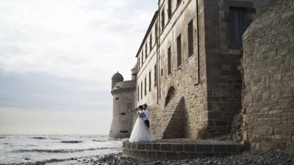 Happy romantic wedding couple standing by the sea near the old castle, photosession outdoors, love and family concept. Action. Bride and groom on the sea shore on their wedding day. — Stock Photo, Image
