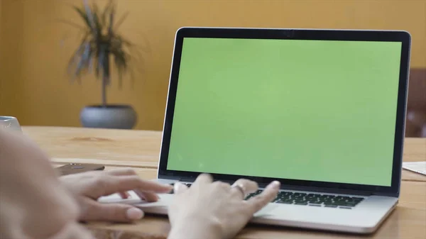 Over the shoulder view of a woman hands using laptop with green screen. Stock footage. Female hands typing on a laptop keyboard, chromakey business, communication, freelance and internet concept