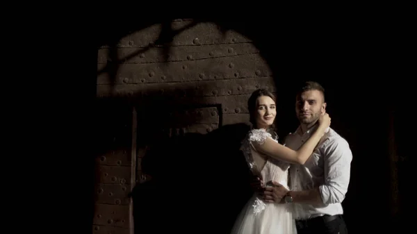 Fabuleux couple de mariage debout contre un mur noir avec l'ombre de la porte métallique. L'action. Portrait de jeune mariée et marié devant un mur sombre . — Photo