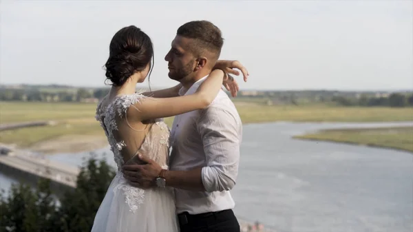 Nehrin arka planında poz veren şık gelin ve damat ve yeşil çayır, aşk ve aile kavramı. Başla. Şehvetli bir düğün çifti sarılıyor ve aşkı paylaşıyor.. — Stok fotoğraf