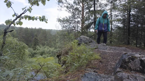 Wandelaar met rugzak wandelen vanaf de rand van het bos heuvel, avontuur en reizen concept. Voorraadbeelden. Een man met een baard in een helderblauw jasje die de berg beklimt in het bos. — Stockfoto