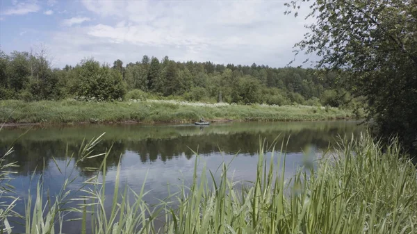 Wunderschöne Sommerlandschaft mit dem Fluss und seinen grünen Ufern und einem Mann, der in einem Schlauchboot schwimmt. Archivmaterial. Fischer fährt Schlauchboot auf dem Fluss. — Stockfoto