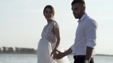 Gelin ve damat nehir kıyısında el ele tutuşarak yürürler. Başla. Gelin ve damadın portresi aşkla dolu gölün arka planında ve parlak gökyüzünde.