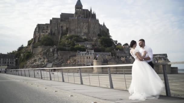 Bela foto de feliz casal recém-casado abraçando. Acção. Noiva em um vestido luxuoso e o noivo em camisa branca e calças pretas na frente do velho castelo bonito na França — Vídeo de Stock