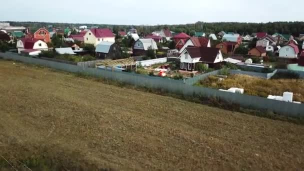 Aerial view of cottage village near the empty field for future building in the end of summer against blue cloudy sky. Stock footage. Beautiful countryside landscape — ストック動画