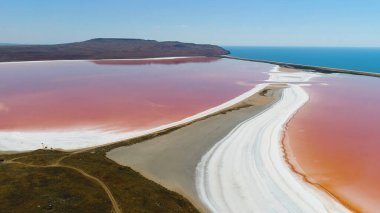 Parlak renkli, ünlü doğal yerin panoramik hava manzarası. Kırım 'da muhteşem bir kıyı şeridi ve arka planda turkuaz deniz bulunan pembe bir göl. Vuruldu. Tuz beyaz kıyıları olan eşsiz pembe göl..
