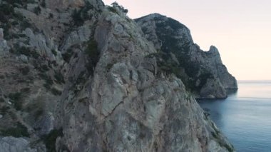 Dağın tepesinde ağaçlar ve arka planda mavi deniz ve gökyüzü olan dev kaya oluşumunun havadan görünüşü. Vuruldu. Dik uçurumlarla nefes kesen doğal deniz manzarası.