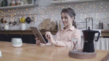 Mutfaktaki ahşap bej masada Ipad 'iyle oturmuş bir şeyler karıştıran çok güzel bir kadın. Stok görüntüleri. Tabletli esmer bir kadının portresi..