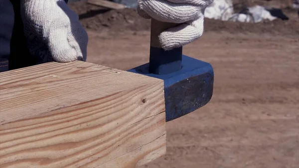 Close up of man hands hitting wooden beam while building the wooden house frame. Clip. Carpenter hammering wooden bars with a sledgehammer.