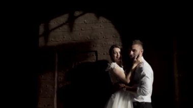 Metal kapının gölgesiyle siyah duvara karşı duran harika bir düğün çifti. Başla. Karanlık duvarın önünde genç gelin ve damadın portresi.