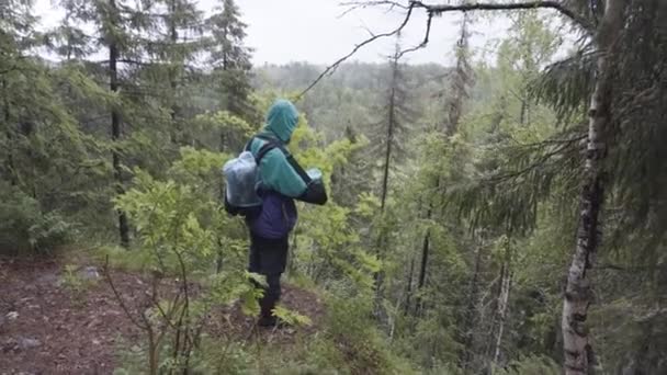 Muž turista s cestovní batoh stojící na okraji vysoké hory během letní trek. Záběry ze skladu. Muž expedice stojí na kopci a dívá se na vrcholky stromů. — Stock video