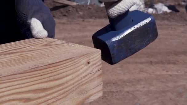 Zbliżenie rąk człowieka uderzających w drewnianą belkę podczas budowy drewnianej ramy domu. Klip. Stolarz młotkuje drewniane pręty młotkiem kowalskim. — Wideo stockowe