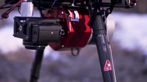 Primer plano de quadcopter rojo y negro de pie en el suelo listo para el vuelo y la filmación de vídeo, concepto de tecnologías modernas. Clip. Nuevo dron con cámara sobre fondo borroso . — Vídeo de stock