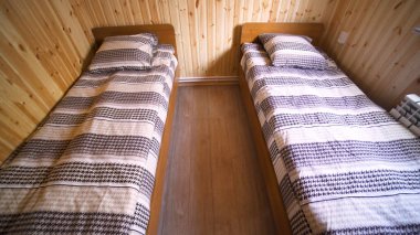 İki yataklı, ucuz konaklama konsepti olan küçük, temiz bir otel odası. - Sanat. Ahşap duvarları, zemini ve iki dar yatağı olan bir oda..