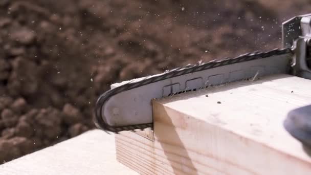 Close-up do trabalhador com serra elétrica cortando feixe de madeira com aparas e poeira voando para os lados. Clipe. Trabalho de carpinteiro, corte de barra de madeira com a serra . — Vídeo de Stock