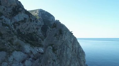 Küçük ağaçlar, yeşil yosunlar ve mavi gökyüzüne karşı deniz kenarındaki büyük kayalıklarla kaplı dağ yamaçlarının muhteşem manzarası. Vuruldu. Güneşin doğuşundaki uçurumun güzel manzarası