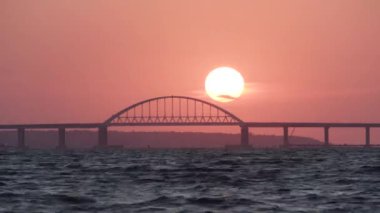 Stunning view of the beautiful sunset over the big river and the bridge, time lapse effect. Shot. Bright golden sun moving towards the horizon above the river.