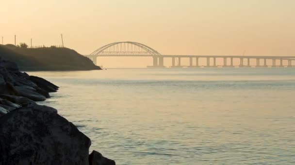 背景には明るい金色の空に海、巨大な美しい橋、石の海岸の息をのむような景色。撃たれた自然の美しさ、時間の経過効果と素晴らしい風景. — ストック動画