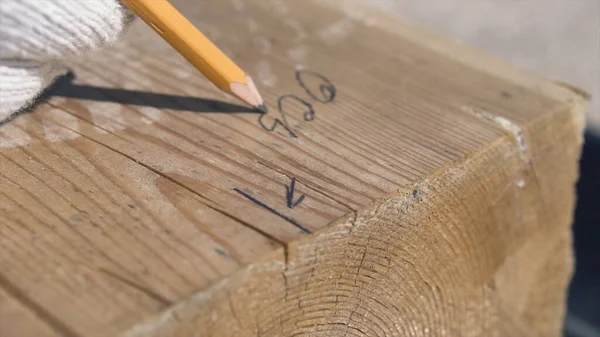 Крупним планом вимірювання і розмітки дерев'яного бруса олівцем. Кліп. Тесляр в білих рукавичках робить позначки на дерев'яній планці з олівцем і лінійкою кутів, процес будівництва будинку . — стокове фото