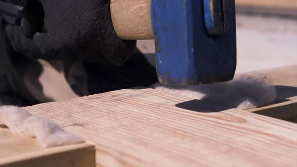 Close up of male carpenter in uniform and white gloves hammering wooden beam while building formwork. Clip. Man worker hitting wide wooden bars with a sledgehammer. — Stock Photo, Image