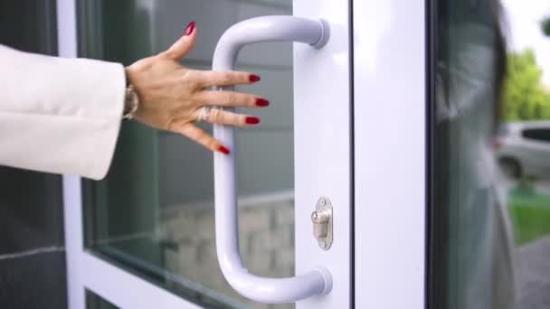 Gros plan de la main de la femme avec de beaux anneaux, montre à son poignet et des ongles rouges ouvrant la porte du bâtiment. L'art. Vue latérale d'une belle femme entrant dans le bâtiment . — Video