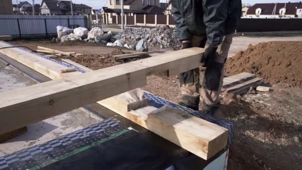 Koncepce nového rámcového domu, jednoho kvalifikovaného, nepoznatelného a zralého stavitele pracujícího na nové dřevěné stavbě. Klip. Dělník drží dřevěný trám a odkládá ho. — Stock video