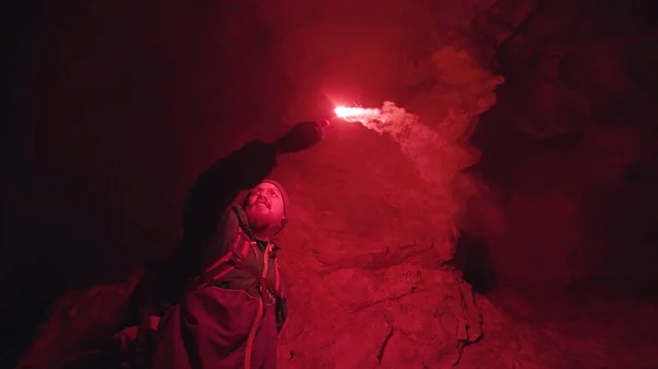 Silhouette dell'uomo con il segnale rosso ardente bagliore camminare su pietre nel buio della grotta, concetto di turismo estremo. Filmati delle scorte. Esploratore maschile all'interno del tunnel sotterraneo . — Foto Stock