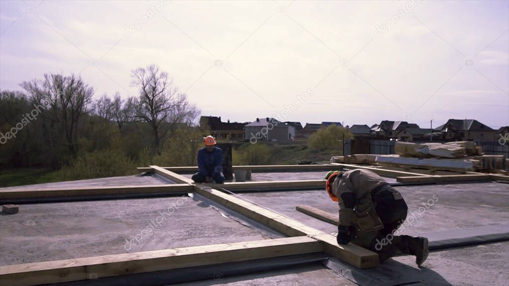 Framing crew rooftop prepairing wooden construction, measuring for better accuracy. Clip. Workers standing on the flat roof of the building and measuring wooden beam with a tape.