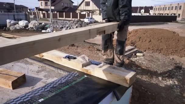 Concepto de nueva casa marco, un constructor calificado, irreconocible y maduro que trabaja en la construcción de nuevos edificios de madera. Clip. Trabajador sosteniendo viga de madera antes de ponerlo abajo . — Vídeo de stock