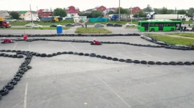 Koruyucu üniformalı ve kasklı Kart yarışçıları güneşli bir günde şehirde eski siyah araba lastikleriyle pistte ilerliyorlar. Medya. Karting Şampiyonası